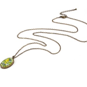 Op de afbeelding: Een gouden ketting met een ovale hanger in groen en geel. De hanger is gemaakt van kleine moza&iuml;ektegels.