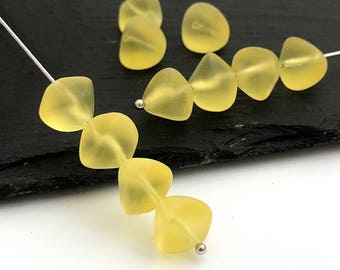 May include: A strand of yellow glass beads in a teardrop shape. The beads are strung on a silver wire.