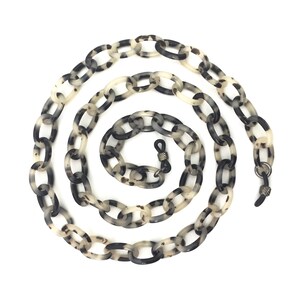 May include: A black and white tortoiseshell patterned plastic chain for glasses. The chain is made of oval links and has metal clasps on each end.