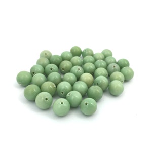 May include: A pile of light green round beads with a hole in the center. The beads are made of a smooth, polished material.