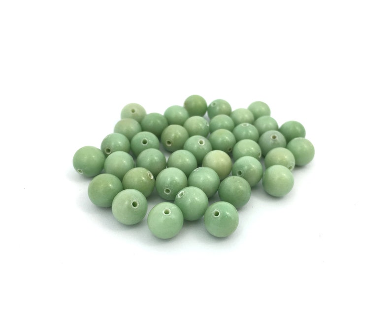 May include: A pile of light green round beads with a hole in the center. The beads are made of a smooth, polished material.