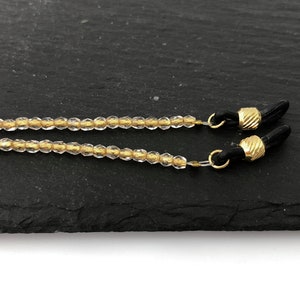 May include: A clear beaded eyeglass chain with gold accents and black rubber ends.