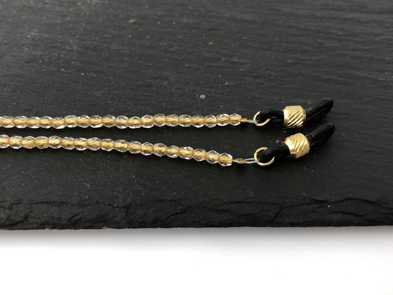 May include: A clear beaded eyeglass chain with gold accents and black rubber ends.
