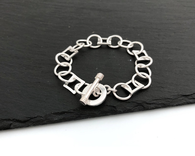 Pu&ograve; includere: Un braccialetto d'argento con chiusura a scatto. Il braccialetto &egrave; realizzato con una catena con maglie rotonde e quadrate alternate.