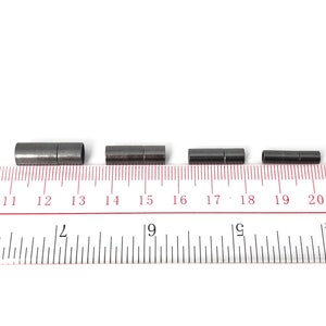 May include: Four black metal cord end caps of varying sizes, measured in inches on a ruler.