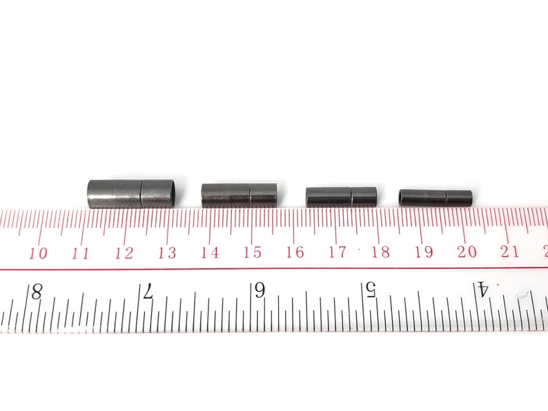 May include: Four black metal cord end caps of varying sizes, measured in inches on a ruler.