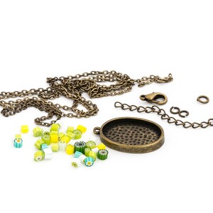 Op de afbeelding: Een ketting van messing met een ronde hanger, een sluiting en springringen. De hanger heeft een getextureerd oppervlak. Er zijn ook kleine, kleurrijke glazen kralen verspreid rond de ketting.