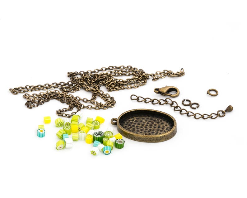 Op de afbeelding: Een ketting van messing met een ronde hanger, een sluiting en springringen. De hanger heeft een getextureerd oppervlak. Er zijn ook kleine, kleurrijke glazen kralen verspreid rond de ketting.