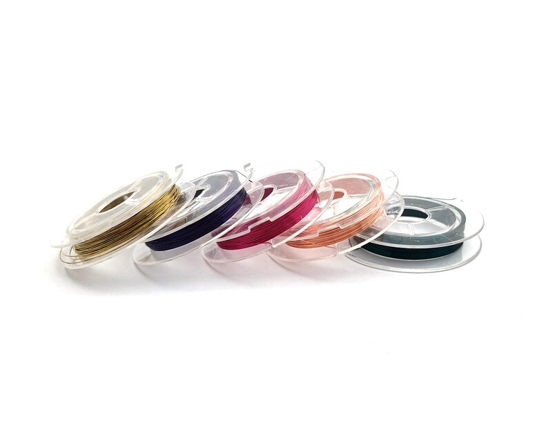 May include: Six spools of wire in different colors, including gold, purple, pink, copper, green, and black. The spools are made of clear plastic and are arranged in a row.