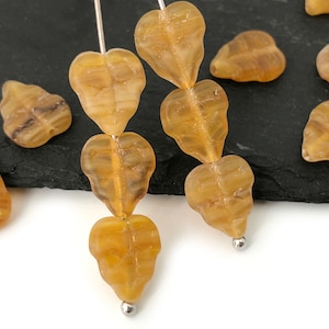 Può includere: Una collana di perline di vetro ambrato a forma di foglie. Le perline sono infilate su un filo d'argento e hanno un aspetto traslucido leggermente nuvoloso.