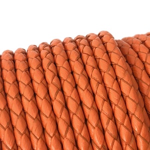 Puede incluir: Primer plano de un carrete de cord&oacute;n de cuero trenzado naranja. El cord&oacute;n est&aacute; enrollado apretado y tiene un acabado liso y pulido.