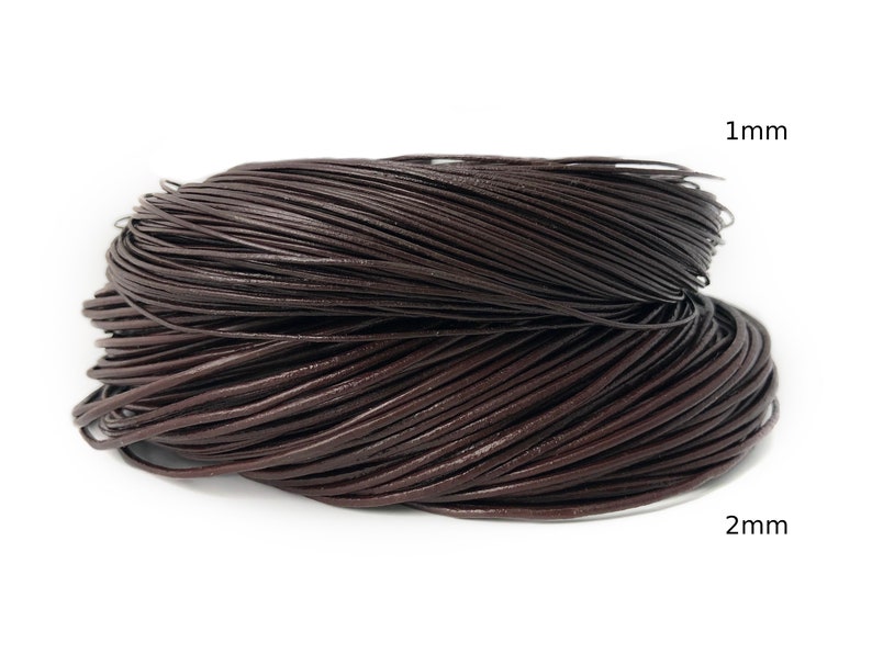 Puede incluir: Dos bobinas de cord&oacute;n de cuero marr&oacute;n oscuro, una etiquetada como 1 mm y la otra como 2 mm. Los cordones est&aacute;n enrollados firmemente, mostrando una textura suave y consistente. Ideal para la fabricaci&oacute;n de joyas y manualidades.