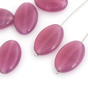 Puede incluir: Un grupo de seis cuentas de vidrio ovaladas, translúcidas y de color rosa. Las cuentas tienen un acabado liso y pulido y están enhebradas en un alambre plateado.