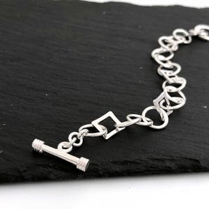 Pu&ograve; includere: Un braccialetto d'argento con chiusura a scatto e una catena composta da quadrati intrecciati.