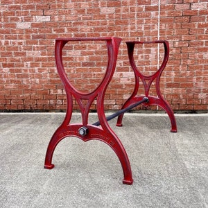 May include: Red cast iron table legs with a distressed finish. The legs are arched and feature a crossbar for stability. The text "JOS CASTING CO CINCINNATI OH" is visible on the legs. The legs are designed for a table.