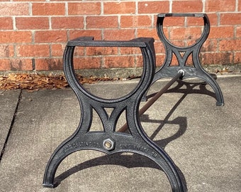 May include: Two black metal table legs with a connecting rod. The legs are marked "U.S. CASTING CO. CINCINNATI, OH."
