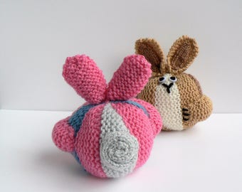May include: Two knitted bunny rabbits, one pink with blue and grey accents, and the other brown with white accents.