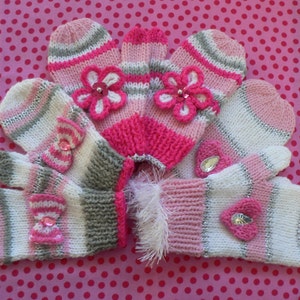 May include: A set of knitted mittens and a hat in pink, white, and grey. The mittens are decorated with bows and flower accents. Some mittens have silver metallic thread woven into the design.