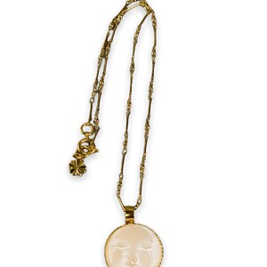 K&ouml;nnte beinhalten: Eine goldene Kettenkette mit einem runden Anh&auml;nger, der ein wei&szlig;es Kamee mit dem Gesicht einer Frau zeigt.