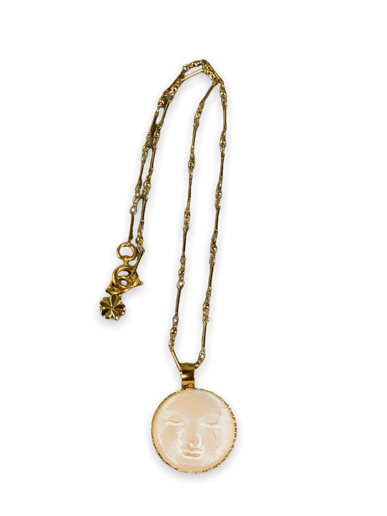 K&ouml;nnte beinhalten: Eine goldene Kettenkette mit einem runden Anh&auml;nger, der ein wei&szlig;es Kamee mit dem Gesicht einer Frau zeigt.