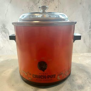 Puede incluir: Una olla de cocción lenta Rival Crock-Pot de color naranja brillante con tapa de cristal transparente y asas laterales negras. El frente tiene una perilla negra con ajustes off, low, high y el texto Rival Crock-Pot Slow Cooker.