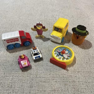Puede incluir: Colección de juguetes Fisher-Price vintage, que incluye un camión rojo y blanco, un autobús escolar amarillo, un coche de policía, un coche rosa con el logo de McDonald's, un reloj y un personaje de patata con sombrero.