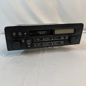 May include: A black Honda car stereo with buttons for AM/FM, CD/Tape, and seek/skip functions. The stereo has a digital display and a volume knob. The text "HONDA" and "Dolby B NR" are visible on the faceplate.
