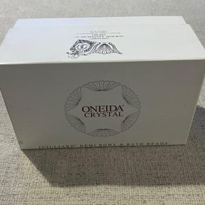 May include: A white rectangular box with the words "ONEIDA CRYSTAL" in a circular design. The box also features the text "JUILLIARD DEMI BOWL & BATH BEADS."
