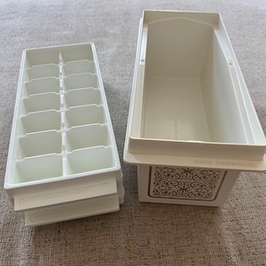 May include: Off-white vintage ice cube tray and ice server. The ice cube tray has 16 individual compartments. The ice server has a rectangular shape with a decorative gold design on the front. The words "ICE SERVER" are printed on the front.