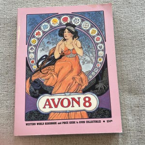 Op de afbeelding: Een softcover boek getiteld AVON 8, Western World Handbook and Price Guide to Avon Collectibles. De kaft toont een illustratie van een persoon met lang donker haar in een oranje jurk, omlijst door een cirkelvormige rand met kleine bloemiconen.