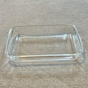 May include: A rectangular clear glass baking dish with rounded corners and integrated handles on the short sides. The dish features smooth, transparent walls and a flat base, designed for oven use and food preparation in a kitchen setting.