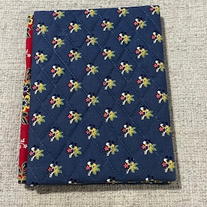 May include: A quilted book cover with a navy blue floral pattern. The cover features a repeating pattern of yellow, pink, and green flowers. The spine is red with a yellow and white floral design.