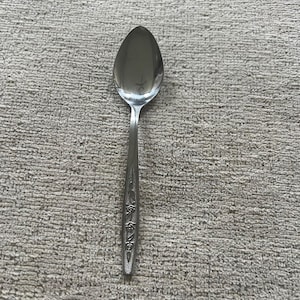 Könnte beinhalten: Ein Edelstahl-Löffel mit floralem Muster am Griff. Der Löffel hat eine abgerundete Schüssel und einen langen, schlanken Griff. Der Löffel ist zum Essen und Servieren von Speisen bestimmt.