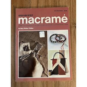 May include: A vintage book titled "STEP-BY-STEP macramé" by Mary Walker Phillips. The cover is a reddish-brown color with the title in large white letters. The book features illustrations of macramé projects, including bracelets and a handbag.