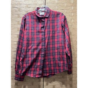 Puede incluir: Una camisa a cuadros roja y azul marino con mangas largas. La camisa está colgada de una percha. El cuello tiene una pequeña etiqueta blanca con texto negro. La camisa está hecha de tela tejida.