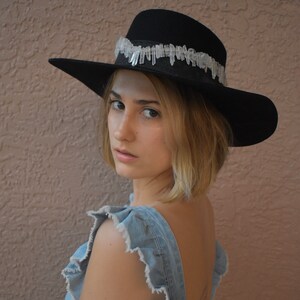 May include: A woman wearing a black felt hat with a crystal trim and a denim overall dress.