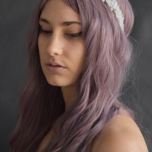 May include: A woman with long, wavy, purple hair is wearing a crystal crown headband. The crown is made of clear quartz crystals.
