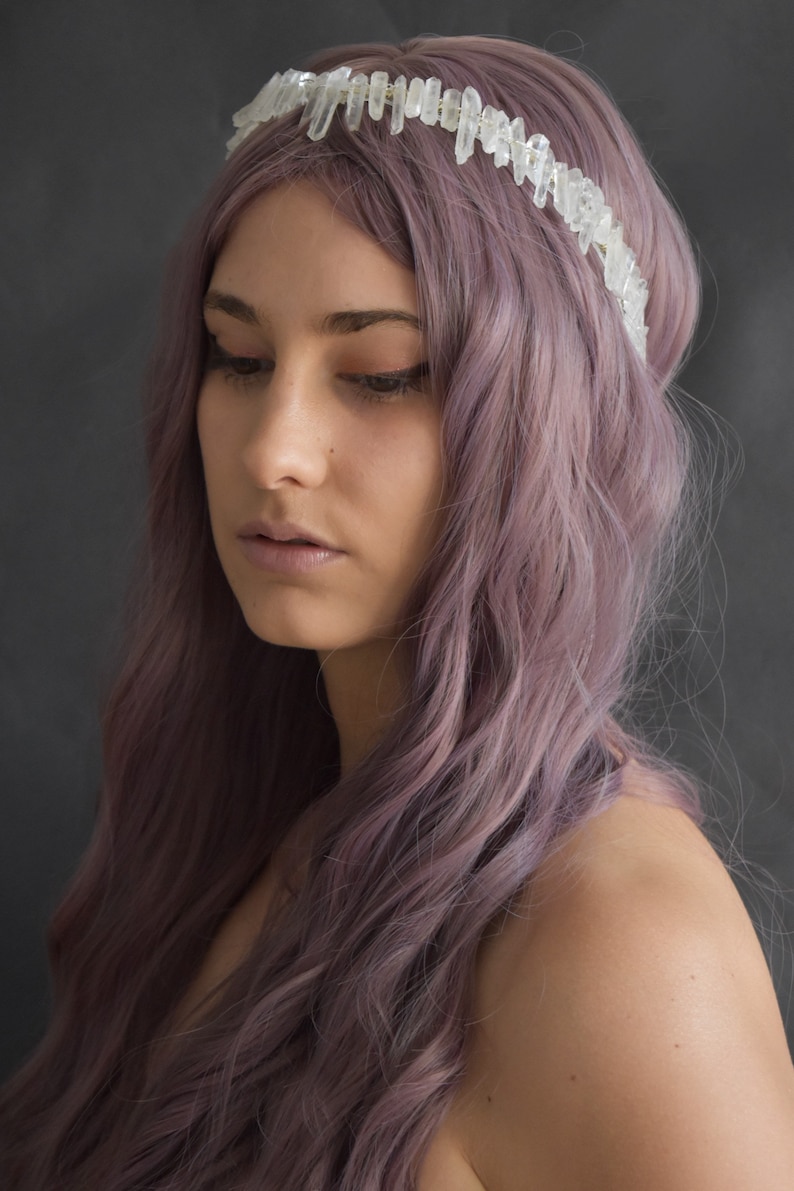 May include: A woman with long, wavy, purple hair is wearing a crystal crown headband. The crown is made of clear quartz crystals.