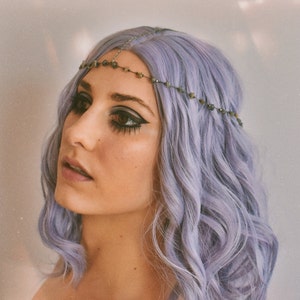 Pode incluir: Uma mulher com cabelo lavanda está usando uma corrente de cabeça com contas de pedras cinza escuro. A corrente é de prata e tem um design delicado.
