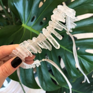 May include: A white crystal quartz headband with a silver wire and white ribbon ties. The headband is made of many small, clear quartz crystals.