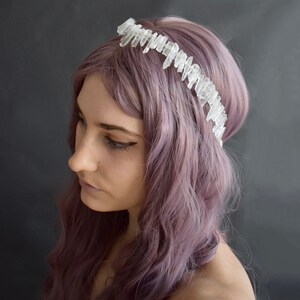 May include: A woman with purple hair wears a crystal crown headband. The crown is made of clear quartz points.