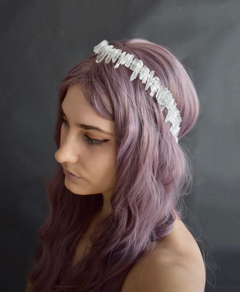 May include: A woman with purple hair wears a crystal crown headband. The crown is made of clear quartz points.