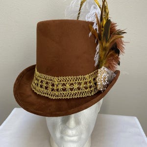 May include: A brown top hat with a gold filigree band and decorative feathers. The hat features a cluster of brown, white, and yellow feathers and a jeweled accent. This formal hat is suitable for costume or special events.