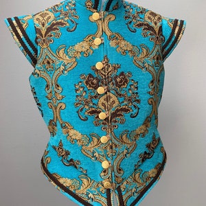 May include: A turquoise sleeveless vest with a gold and brown damask pattern and gold buttons. The vest has a mandarin collar and a pointed hem.