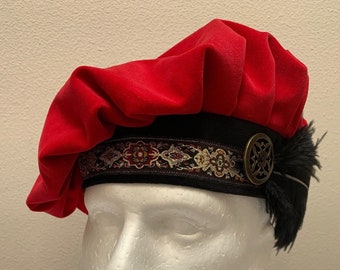May include: A red velvet beret with a black band and a gold-toned decorative button. The band has a patterned design in gold, red, and black.