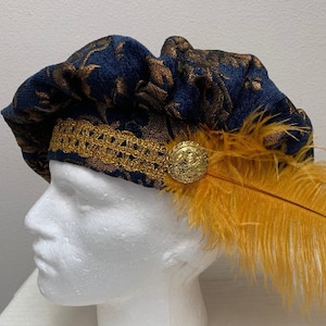 Op de afbeelding: Een blauwe hoed met gouden patroon, een gouden knoop en een gele veer.