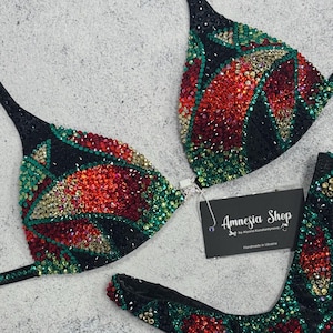 Puede incluir: Bikini negro con adornos de cristal rojo, verde y dorado. La parte superior del bikini tiene forma de triángulo y la parte inferior es de estilo de corte alto. El bikini está hecho a mano en Ucrania. La etiqueta dice "Amnesia Shop by Anya Konstantynovych".