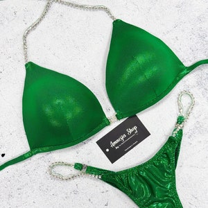 May include: Sparkly green bikini with crystal embellishments. The bikini top has a halter style strap and the bottom is a cheeky cut. The bikini is labelled "Amnesia Shop".