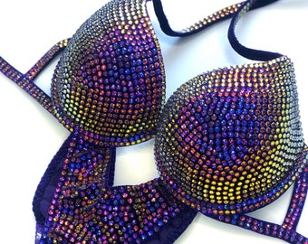 May include: A purple, sequined bikini with iridescent rhinestones in a swirling pattern. The bikini top has a plunging neckline and adjustable straps. The bikini bottom has a high-cut leg.