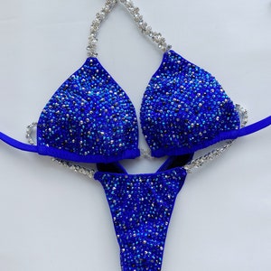 May include: A royal blue bikini with silver embellishments. The bikini top has a halter style strap and the bottom is a cheeky cut.